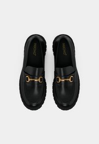 Mocassins en cuir noir avec une boucle en forme de fer à cheval en ton doré, dotés d'une épaisse semelle en caoutchouc noir et d'une finition lisse.