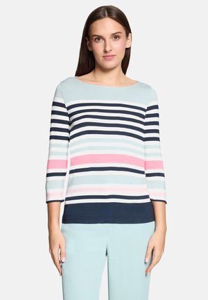 Femme portant un pantalon bleu clair et un haut à manches longues rayé avec des rayures horizontales bleu marine, blanches, roses et bleu clair.