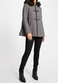Cappotto a scacchi bianco e nero con colletto in pelliccia sintetica, dotato di chiusure a toggle e tasche laterali. Abbinato a jeans skinny neri e stivali con tacco.