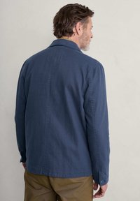 Marineblaue Jacke mit lässigem Schnitt, geknöpften Manschetten und glatter Textur, ausgestattet mit einer Rückenpasse und subtilen Nähten.