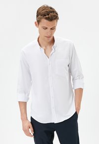 Witte button-up shirt met een zak en lange mouwen die tot de ellebogen zijn opgerold. De stof lijkt glad en lichtgewicht, met een klassieke kraag.