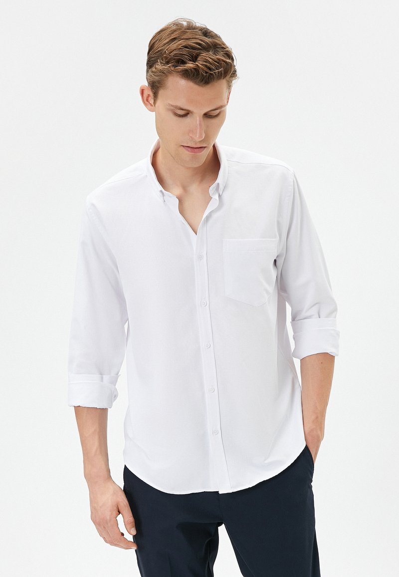 Witte button-up shirt met een zak en lange mouwen die tot de ellebogen zijn opgerold. De stof lijkt glad en lichtgewicht, met een klassieke kraag.