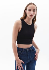Top corto nero a costine con collo alto e senza maniche. Abbinato a jeans in denim blu a vita alta con tasche frontali.
