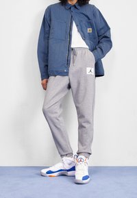 Blå vadderad jacka, grå sweatpants med logotyp, och vita sneakers med blå och orange accenter. Slätt tyg, avslappnad passform och tryckknappsstängning.