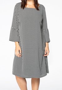 Šaty s černo-bílým skotským vzorem houndstooth, s tříčtvrtečními zvonovými rukávy a čtvercovým výstřihem, vyrobené z lehkého materiálu.