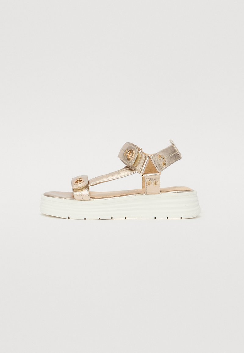 Goldene metallische Plattformsandalen mit verstellbaren Riemen, die runde Akzente und eine strukturierte weiße Sohle aufweisen. Minimalistisches Design mit breiter Form.