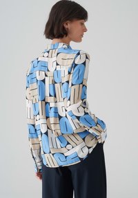 Camicia a maniche lunghe in tessuto satinato con un motivo geometrico nei colori blu, beige e nero. Orlo arrotondato e polsini con bottoni.