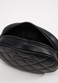Bolso de piel negra acolchada con forma redondeada, cuenta con un cierre de cremallera y un interior suave. Etiqueta "ALDO" visible en el interior.