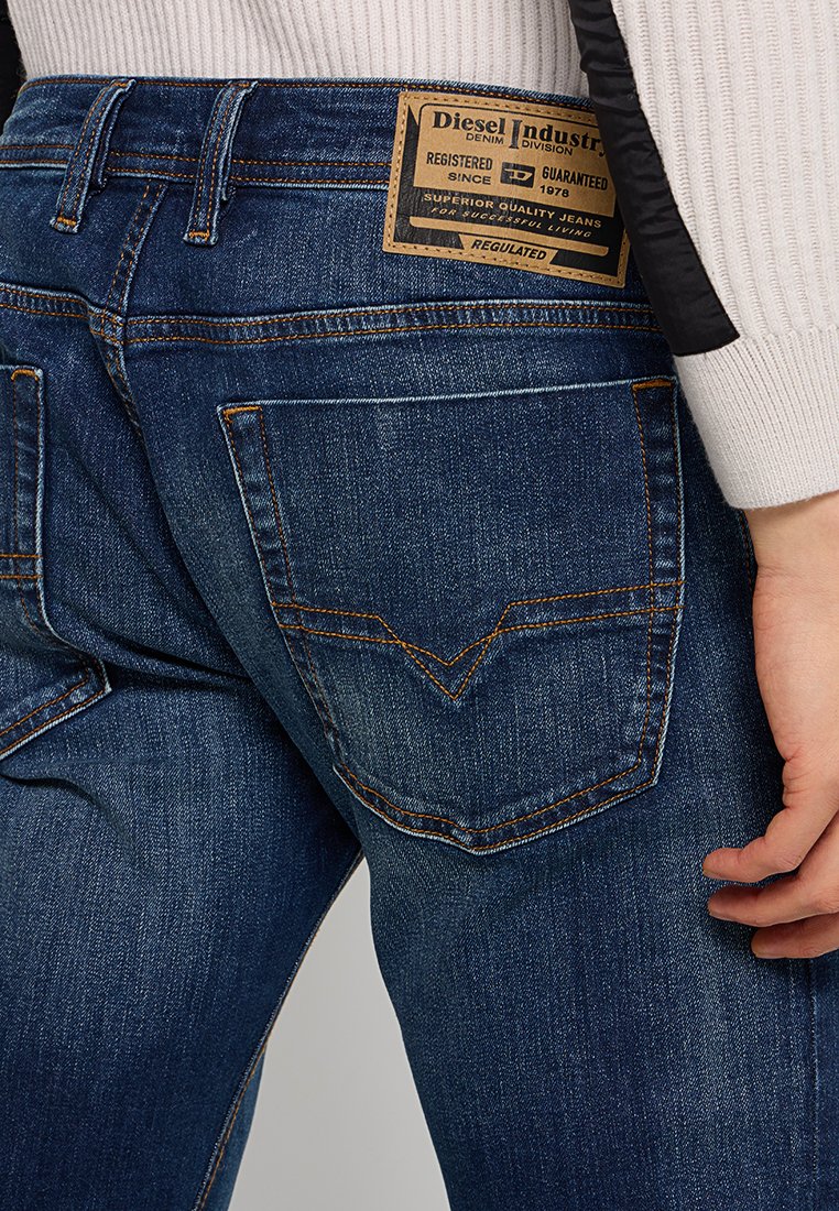 Dunkelblaue Denim-Jeans mit einer verblassten Textur, ausgestattet mit einem rechteckigen Lederetikett am Bund und genähten Gesäßtaschen.