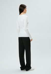 Maglione bianco a coste con maniche lunghe, silhouette aderente, abbinato a pantaloni neri a gamba larga e sneaker bianchi. Design minimalista.