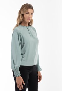 Langærmet lyseblå bluse med en samlet halsudskæring og rynkede, voluminøse manchetter. Glat stof med en afslappet pasform.