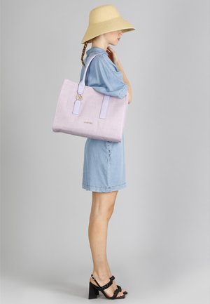 Lilla tote taske med tekstureret stof, dobbelt håndtag i toppen og med guldaccent. Båret over en denimkjole, suppleret med en bredskygget hat.