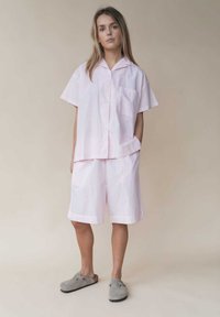 Chemise rose clair à manches courtes et shorts assortis en tissu doux et texturé. Dispose d'une poche avant et d'une coupe décontractée. Chaussures à enfiler grises.