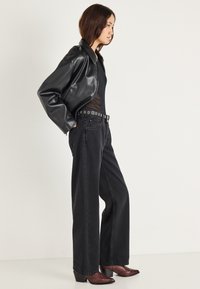 Čierna kožená bunda, priliehavé čierne body, široké čierne džínsy a hnedé členkové čižmy so špicatou špičkou, doplnené o kovový opasok.