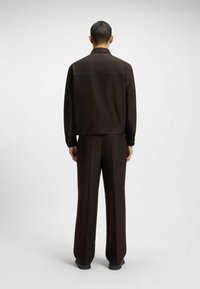 Brown woven suit jacket and pants, back view; relaxed fit, long sleeves, straight-leg trousers, minimal detailing, smooth texture.