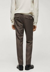 Pantaloni beige su misura con una texture liscia, dotati di due tasche posteriori con bottoni e un design a gamba affusolata. Indossati con un maglione di colore chiaro.