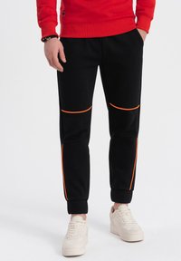 Sorte sweatpants med orange detaljer, med en tapered design, ribbede manchetter og teksturerede knæpaneler lavet af blødt stof.