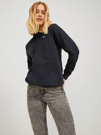 Felpa nera con tasca frontale e cordino, caratterizzata da un piccolo logo sul petto. Abbinata a jeans skinny grigi e texturizzati.