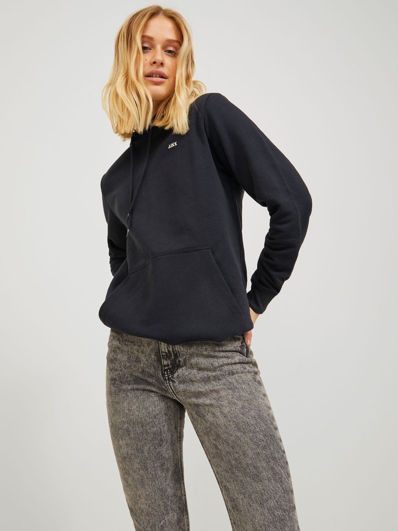 Felpa nera con tasca frontale e cordino, caratterizzata da un piccolo logo sul petto. Abbinata a jeans skinny grigi e texturizzati.
