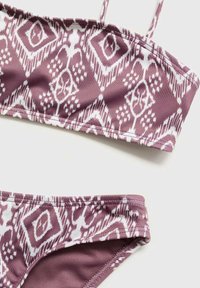 Bikini vrchná časť a spodná časť v mušelínovej farbe s bielym vzorom. Materiál je hladký, s nastaviteľnými ramienkami a elastickými pásmi na okrajoch.