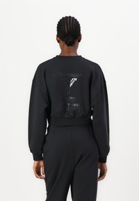 Černá mikina s přiléhavým lemem, oversized rukávy a embosované logo na zadní straně. Jemný a elastický materiál pro pohodlí.