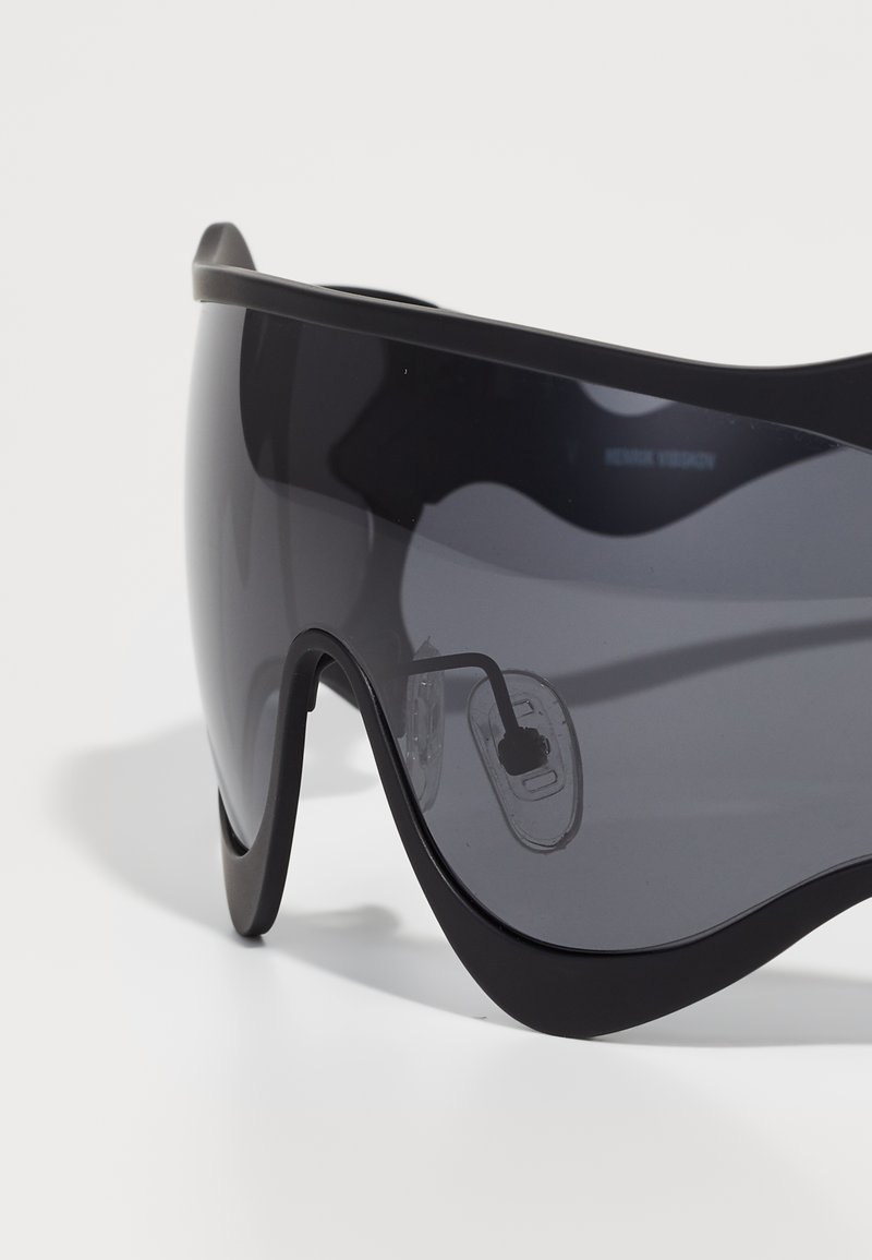 Black sports sunglasses with wraparound design, grey tinted lenses, and clear nose pads. The frame features a smooth, sleek finish.