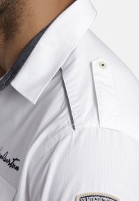 Weißes Hemd mit einem grauen Akzent am Kragen, vertikaler Textur, Knopfdetails an der Schulter und einem gestickten Logo.
