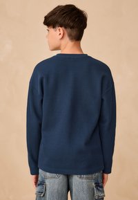 Tumši zils ribots garā piedurkņu krekls ar vaļīgu piegriezumu, apaļu kakla izgriezumu un nolaistām plecu līnijām, kombinēts ar gaiši ziliem cargo džinsiem.