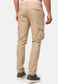 Beige cargo hlače s uskim krojem, koje imaju bočne džepove, dugmad za stražnje džepove i glatku, teksturiranu tkaninu. Uparene s tamnim tenisicama.