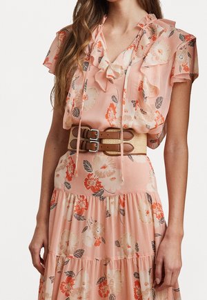 Woman wearing a pink floral dress with ruffled sleeves and a wide beige belt with two brown buckles.