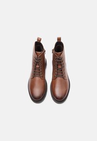 Καφέ δερμάτινα μποτάκια μέχρι τον αστράγαλο με λείο φινίρισμα, στρογγυλή μύτη, κορδόνια μπροστά και βρόχο για εύκολη φόρμα στην πλάτη. Συμβατά με διάφορα στυλ.