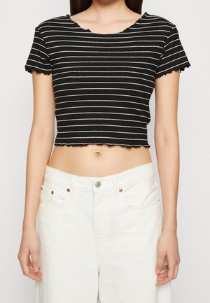 Schwarzes und weißes gestreiftes Cropped-T-Shirt mit rundem Ausschnitt und gewellten Kanten, kombiniert mit weißen, hoch taillierten Jeans. Strukturiert Stoff.