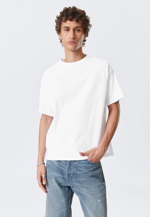 White cotton t-shirt with a round neck and short sleeves, featuring a relaxed fit. Paired with light blue distressed denim jeans.