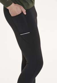 Svarta åtsittande leggings gjorda av elastiskt material, med en sidoficka med en vit accentrand och kontrasterande sömmar.