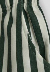 Tessuto a righe con colori alternati verde scuro e bianco sporco; presenta una trama strutturata e un dettaglio in vita con elastico.