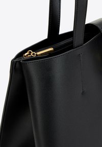 Sac à main en cuir noir avec une texture lisse, doté de poignées doubles et d'une fermeture éclair dorée. Étiquette de marque notable visible sur la fermeture éclair.