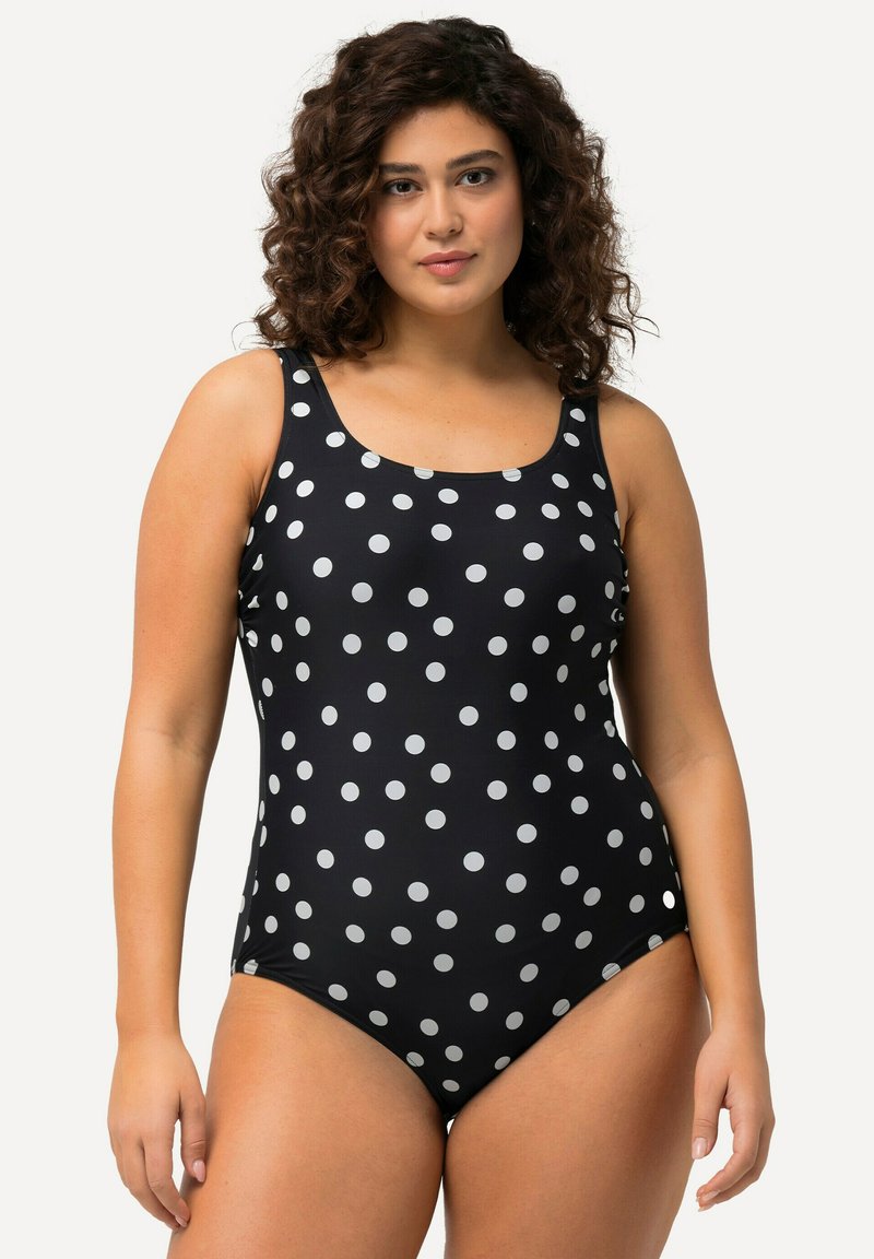 Maillot de bain une pièce noir à pois blancs, avec des bretelles larges et un décolleté en scoop. Confectionné dans un matériau lisse et extensible.