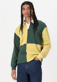 Camisa polo de manga larga en bloques de color verde y amarillo con collar blanco, material de algodón, corte relajado y puños acanalados.