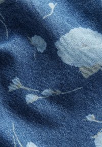 Tejido de mezclilla con un fondo azul y un patrón floral en azul claro y crema. La textura es suave con ligeras arrugas.
