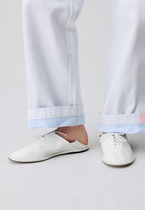 Scarpe in pelle bianca con una superficie liscia, design a profilo basso e allacciatura, abbinate a pantaloni azzurri chiari con risvolti.