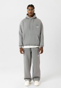 Grijze hoodie met een voorzak en blauwe grafische details, gecombineerd met bijpassende grijze joggingbroek. Beide kledingstukken zijn gemaakt van zachte stof.