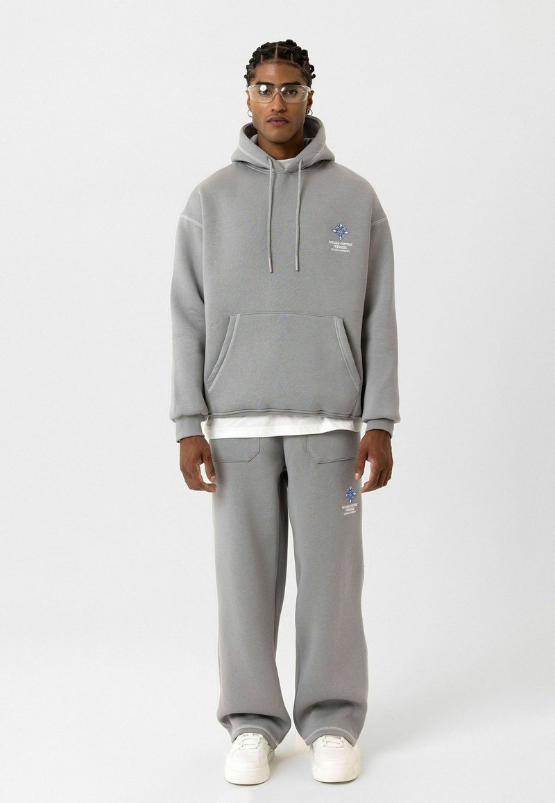 Grijze hoodie met een voorzak en blauwe grafische details, gecombineerd met bijpassende grijze joggingbroek. Beide kledingstukken zijn gemaakt van zachte stof.