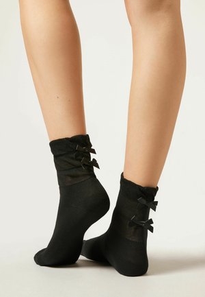 Svarta ankelsockar gjorda av ett genomskinligt material med en volangkant och tre små svarta rosetter på varje sida. Slät textur, åtsittande form.