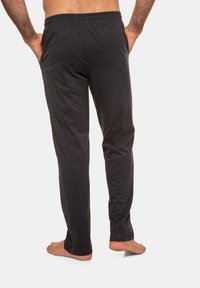 Donkergrijze, zachte sweatpants van stof met een elastische tailleband, taps toelopende benen en geen zichtbare zakken, gezien van achteren.