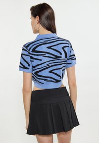 Top in maglia blu tagliato, con un motivo astratto a onde nere, maniche corte e colletto piatto. Abbinato a una gonna nera a pieghe.