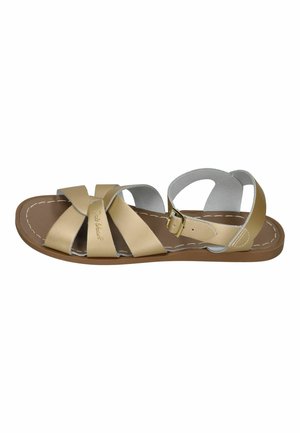 Beige leather open-toe sandal with three front straps, ankle strap with buckle, and brown flat sole with white stitching.