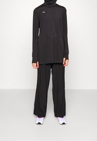 Svart träningsoutfit bestående av en långärmad topp med hög krage och löst sittande byxor, med Puma-logotypen.