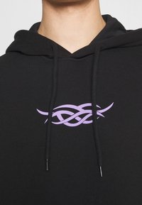 Felpa nera con lacci neri presenta un design centrale a linea intrecciata in stile tribale lavanda sul petto.