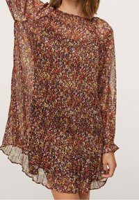 Vestido de mangas largas con estampado floral y una forma holgada y fluida. Fondo oscuro con pequeñas flores amarillas y blancas; tejido ligero y transparente.