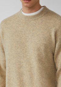Beige gebreide trui met een geribbelde ronde hals en lange mouwen, gemaakt van zacht materiaal, met een gestructureerde oppervlakte.